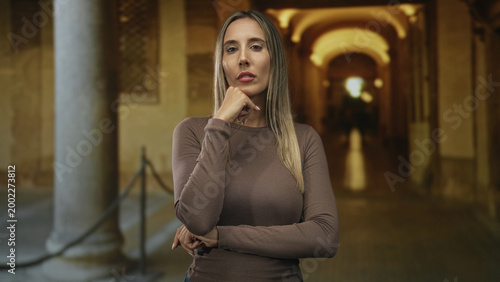 Foto Woman with hand on chin and crossed arms in old town building corridor under arched walkway; contemplation