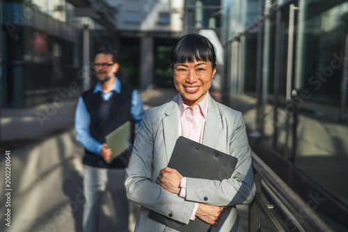 Tablou pe pânză Confident businesswoman smiling with colleague outdoors at corporate building