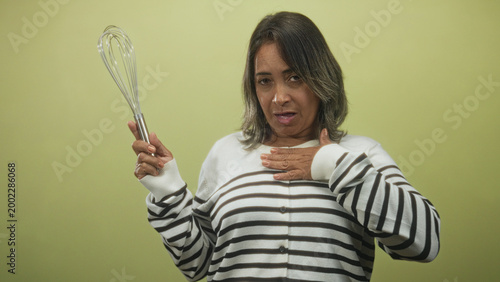 Slika na platnu Woman holding whisk with hand on chest, striped sweater visible, expressive gasp gesture in studio; surprise