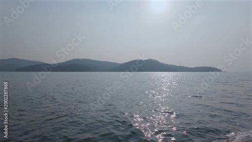 Sunrise over calm waters with distant mountains and a hazy sky in the early morning