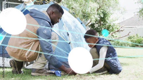 Father and son placing stake, securing blue tent for camping, teal overlays sweeping hands