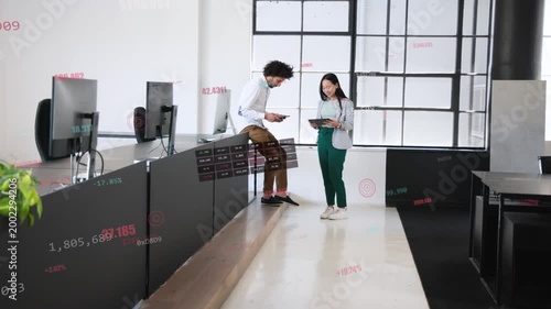 Two coworkers leaning showing tablets walking reviewing business charts with overlays on tablets