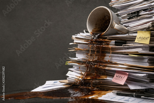 An overflowing stack of documents with spilled coffee on the table. Space for text.