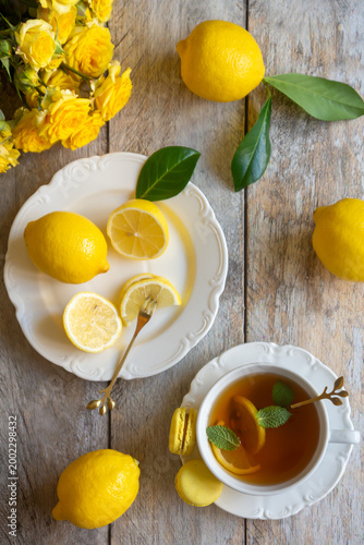 фотографія On the table are ripe lemons and a cup of tea in a white porcelain cup, which also contains a lemon