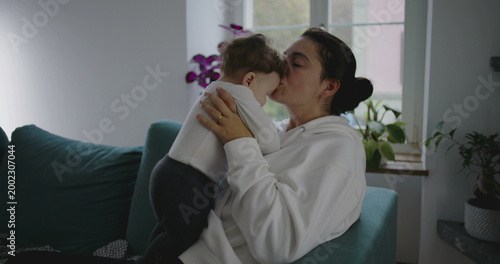 Photos Mother kissing baby affectionately while holding him close in cozy home setting,