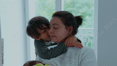 Fotografie Young boy embracing his mother near window, wrapping arms around her neck with e
