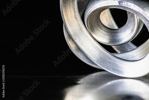 Closeup of bent aluminum rods on a reflective metal surface, showing aluminum structure and plasticity as raw material of light metal industry