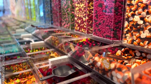 Abundant assortment of colorful, sugary gummies and jellies displayed in clear dispensers at a candy store, with scoops ready for a pick and mix selection of sweet confectionery