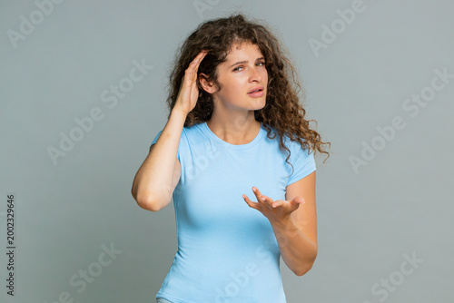 Fotografía Young woman holding hand near ear gesture indicating difficulty hearing clearly, confused emotional reaction