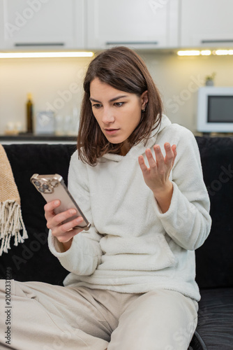Foto Young woman at home reads negative phone alert frowns whispers why did this happen feels shock and fear