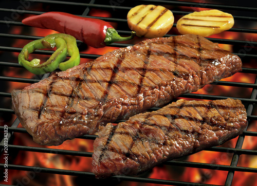 Tableau sur toile Grilled flank steak on a barbecue rack with flames, potatoes and peppers garnish