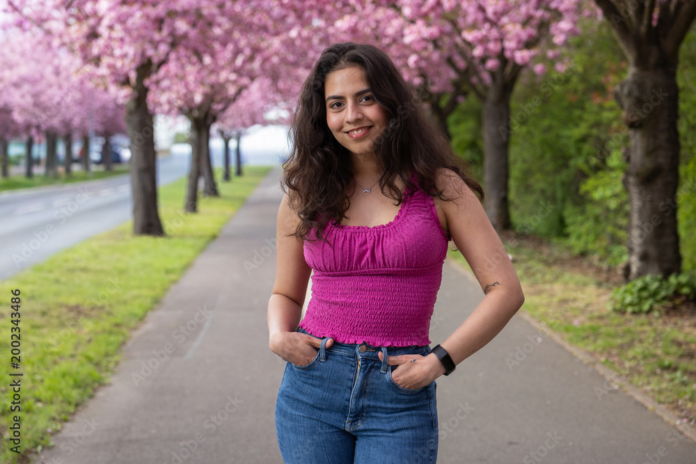 Fototapeta premium Young woman portrait with cherry blossom avenue in spring city background