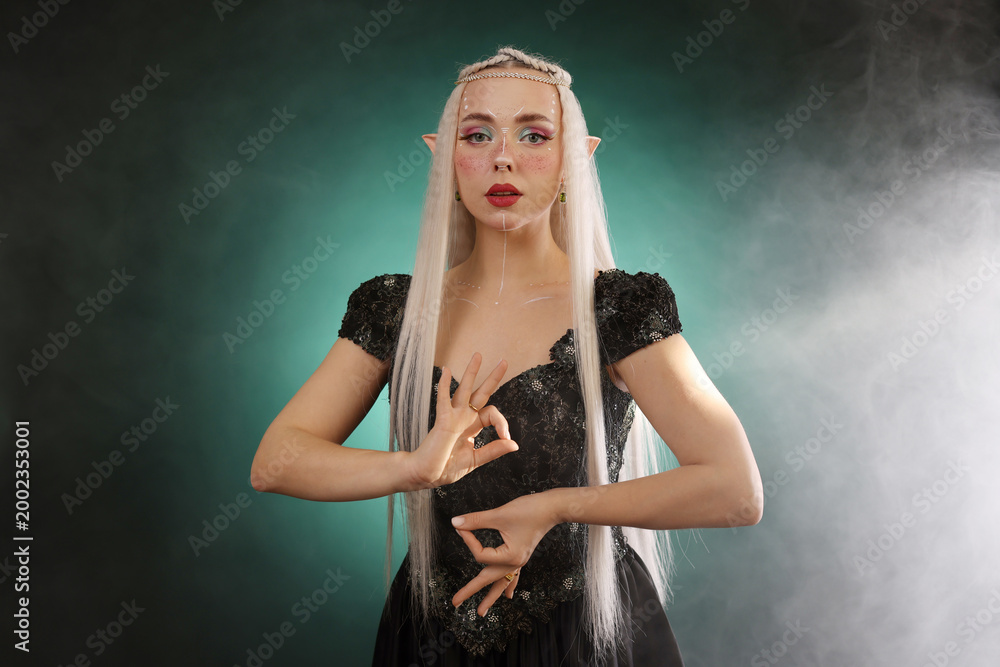 Fototapeta premium Beautiful girl dressed as elf on dark background with smoke