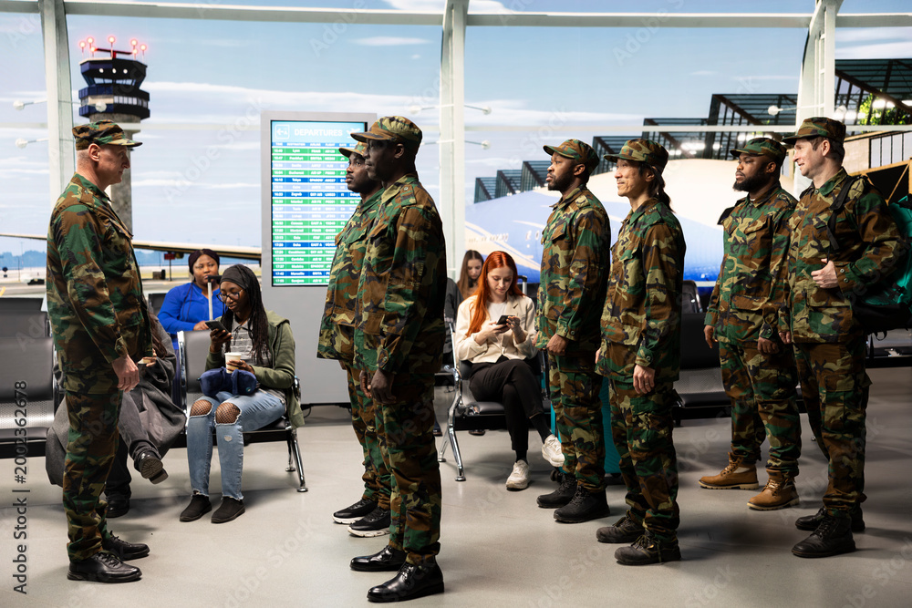 Fototapeta premium Receiving orders, formation and military troops team with veteran standing in airport terminal. Standing at attention, camouflage uniforms and multiracial army squad in airport hub