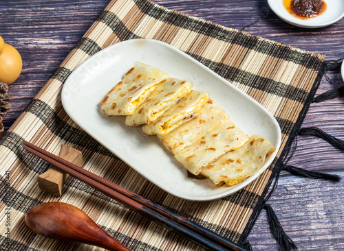 Traditional taiwanese egg crepe dan bing sliced on a white plate with chopsticks and chili sauce