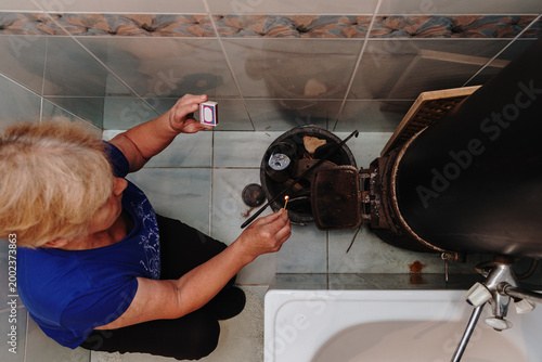 A mature Caucasian woman lights a stove with a match.