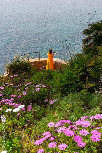 Woman in yellow dress at scenic coastal viewpoint with flowers
