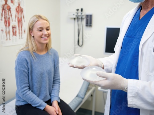 A woman consults with a doctor who is holding breast implants in a medical office. Concept of cosmetic surgery and patient consultation.