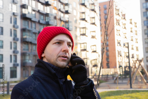 Man talking on smartphone outdoors in winter. Guy wearing red hat and coat uses cellular phone on street. Communication, technology, mobile lifestyle urban daily routine. conversation with scammers
