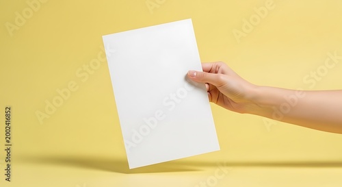 Hand Holding Blank White Paper Mockup on Yellow Background