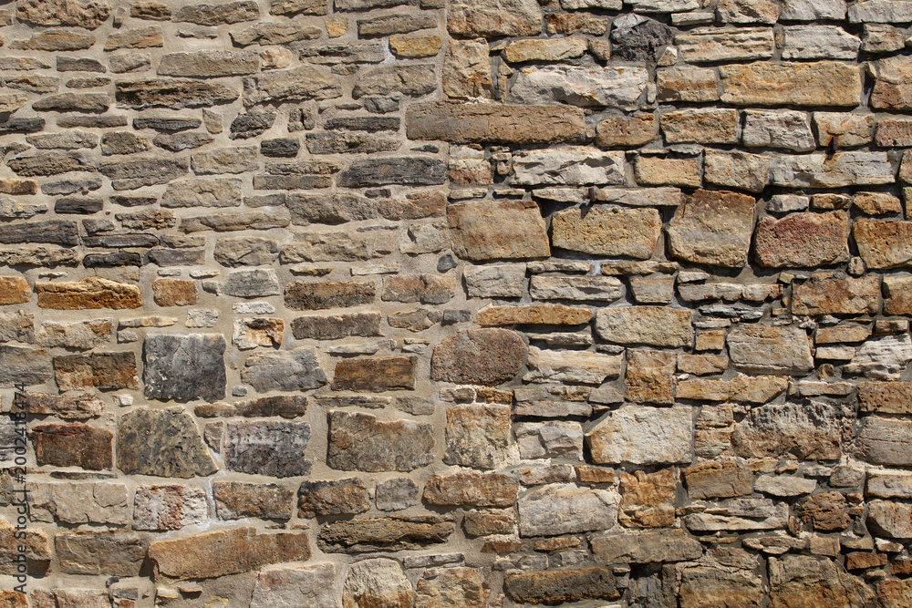 Fototapeta premium Rough stone wall with varied sizes and natural hues. Stones form a sturdy, weathered surface. Textures show age and craftsmanship. Ideal for architectural backgrounds or historical contexts