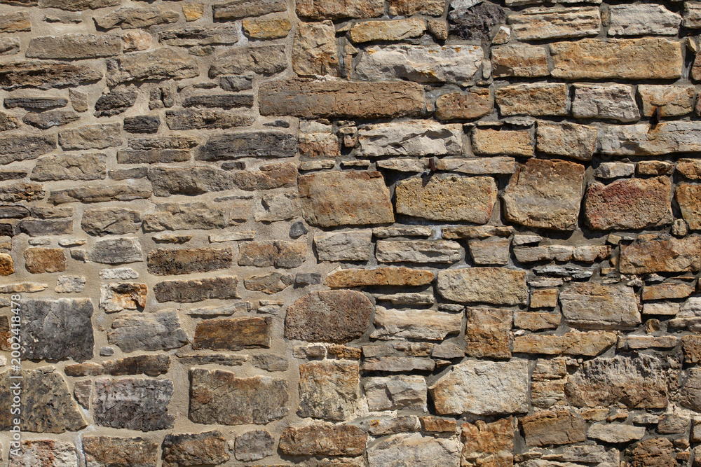 Fototapeta premium Rough stone wall with varied sizes and natural hues. Stones form a sturdy, weathered surface. Textures show age and craftsmanship. Ideal for architectural backgrounds or historical contexts