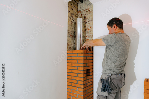 A young man makes brickwork on the chimney of a fireplace.