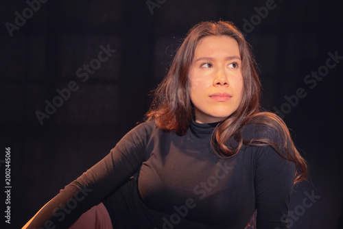 A stunning portrait of a woman in a black turtleneck exuding confidence and elegance, captured in soft lighting against a dark background creating a dramatic effect.