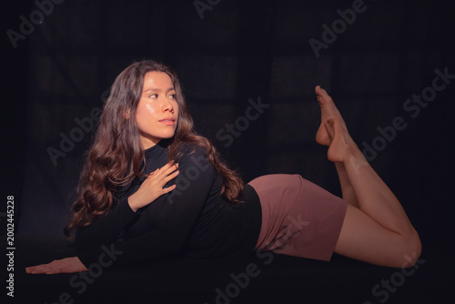 This striking image features a woman gracefully lounging with her hair flowing, dressed in a stylish outfit, evoking confidence and elegance against a dark artistic backdrop.