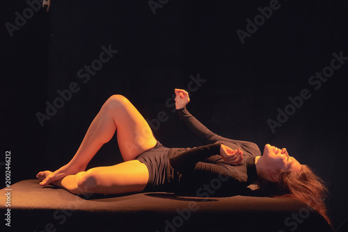 A joyful moment captured as a woman in black attire lays laughing on a bed, with soft lighting illuminating her relaxed pose, evoking feelings of joy, comfort, and carefree expression.