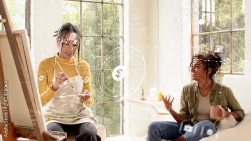 Artist pausing at easel as friend showing object and talking, HUD graphics showing finance data