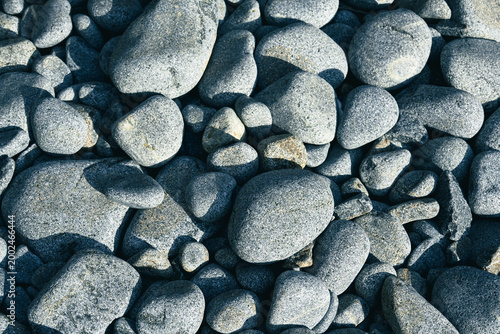 Obraz na plátně A cluster of smooth gray pebbles lies scattered along the shoreline, shaped by the constant wash of sea waves under soft sunlight