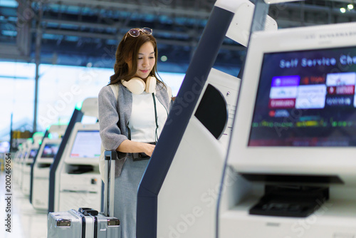 Asian woman using airport self service check in kiosk