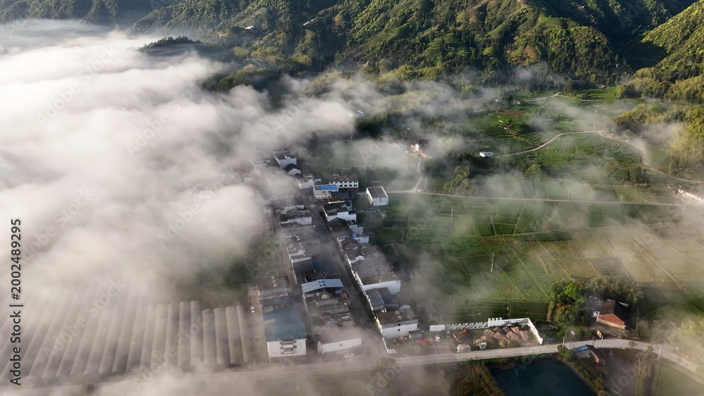Fototapeta premium Aerial view of a rural village nestled among misty mountains and terraced farmland at dawn