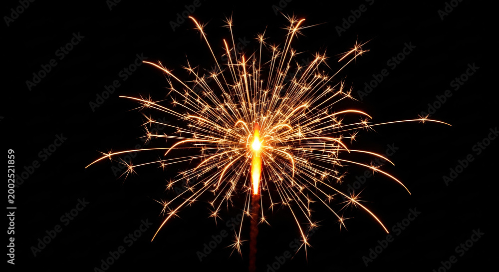 Obraz premium Brightly Burning Sparkler Igniting Golden Fiery Particles Against a Dark Black Background