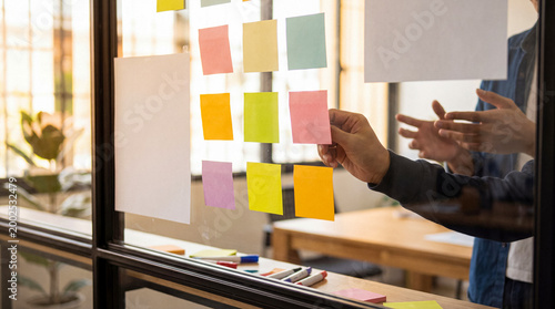 Foto Hands arranging colorful sticky notes on a glass wall during a creative business brainstorming meeting in an office