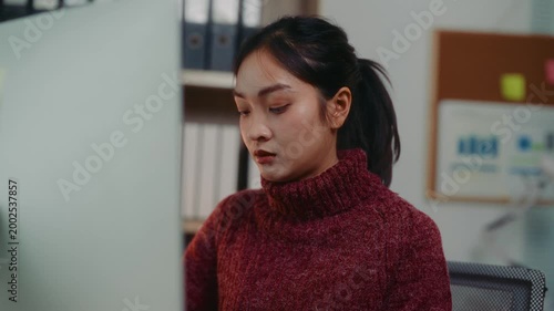 Serious asian woman typing on keyboard and looking at a computer monitor. Focused female employee working late at night in a modern office
