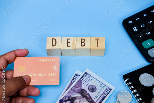Konstfotografi Debt concept: hand holding credit card, money, coins, calculator on blue backgro