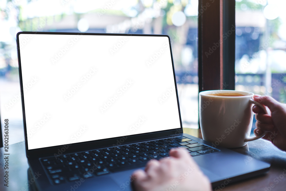 Fototapeta premium Mockup image of a woman working on laptop computer with blank white desktop screen while drinking coffee in cafe