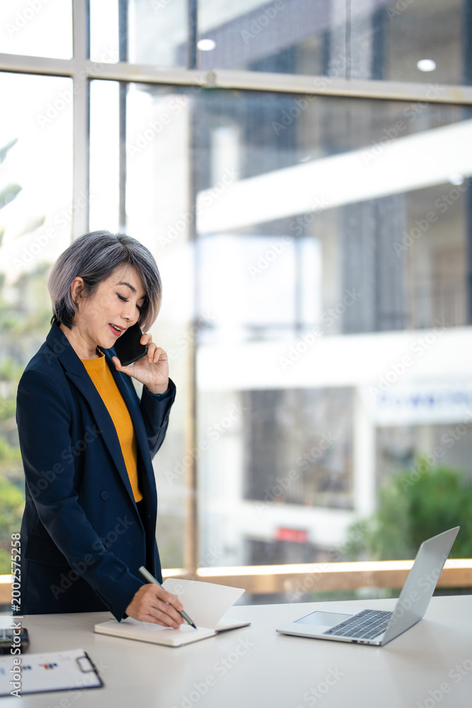 Obraz premium Businesswoman talking on smart phone and taking notes working in corporate office.