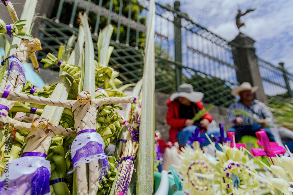 Ταπετσαρία Close-up of Jesus Christ figures woven from palm leaves, with artisans selling their crafts outside a church during Holy Week