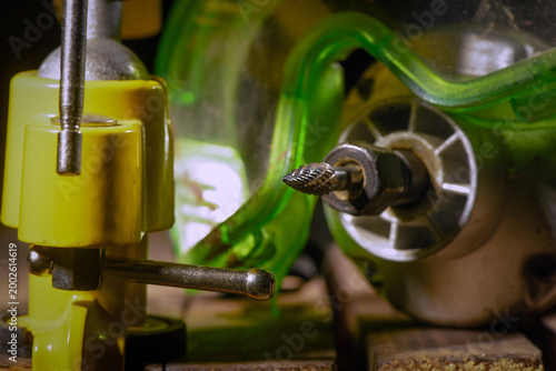 Electric straight grinder with metal burr bit fixed in clamp on wooden workbench table close up background.