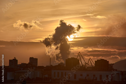 A gijon sunset obscured by industrial smoke, casting a dramatic silhouette