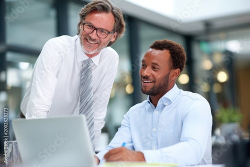 Experienced senior executive and younger businessman talking together in modern corporate office during professional business meeting discussion.
