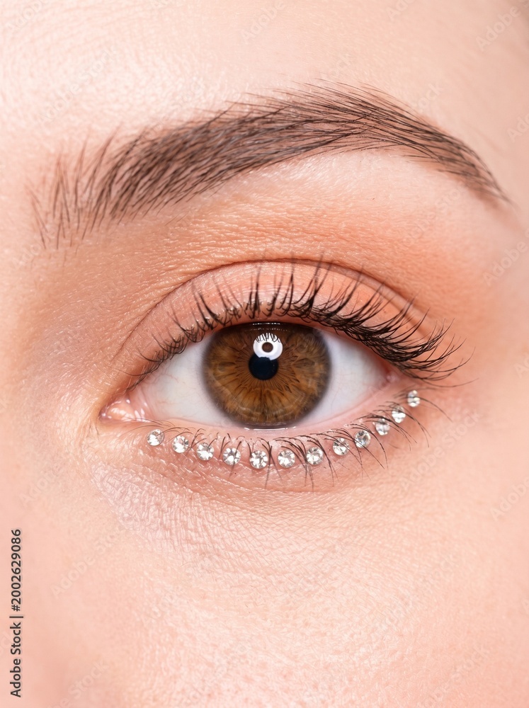 Fototapeta premium Macro of a single human eye with tiny crystal rhinestones glued along lower lash line, surreal editorial beauty