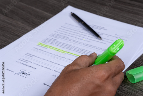 Hand holding green highlighter over contract on a desk with pen