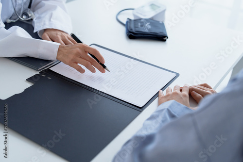 Doctor explaining treatment plan and obtaining informed consent while patient signing consent form in hospital.