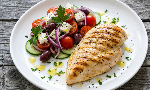 Grilled chicken breast served with greek salad on white plate feta cheese red onion light meal balanced diet tomatoes