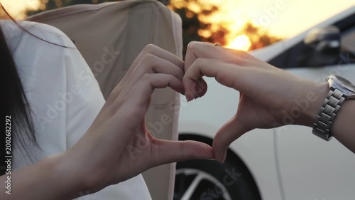 Happy couple making heart gesture with fingers in sun park. Heart with fingers symbol Valentine's Day.