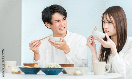 Bild auf Leinwand A young Asian couple eating at their home dining table (the food is unappetizing, the seasoning is bad)